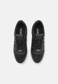 Sneaker nere con una parte superiore testurizzata, materiale sintetico liscio, lacci piatti e dettagli dorati, il tutto su una suola in gomma bianca.