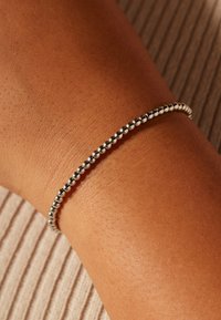 Zilveren armband met kralen om een pols, met bolvormige kralen in een gelijkmatig patroon. Huidtint contrasteert met de metallic textuur van de armband.