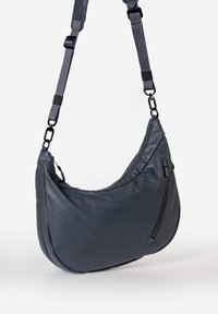 Graue, weiche Schultertasche mit kurvenförmigem Design, Reißverschlussfach und verstellbarem Tragegurt mit metallenen Hardware-Akzenten.