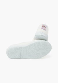 Zapatillas de tela blanca con una suela de goma texturada y un parche redondo con un diseño de mono, que indica la marca y el origen.