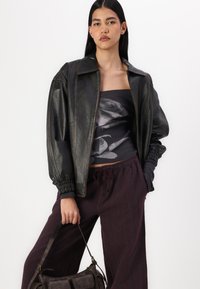 Black leather bomber jacket with a structured collar, cinched sleeves; paired with a gray floral top and maroon striped wide-leg pants.