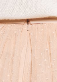 Jupe en tulle pêche avec une finition texturée, dotée d'une fermeture éclair dissimulée à l'arrière et de petits motifs d'étoiles blanches sur l'ensemble.