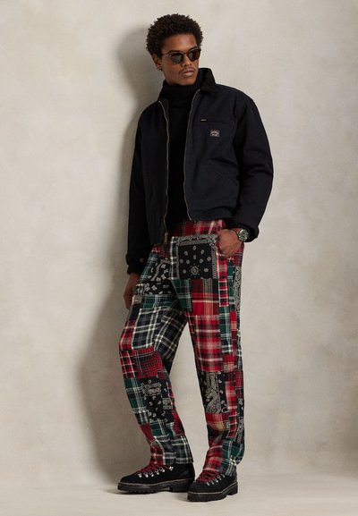 Czarna kurtka na zamek noszona na czarnym golfie, zestawiona z wielokolorowymi spodniami patchworkowymi z wzorami w kratę i kwiaty. Czarnymi butami dopełniono stylizację.