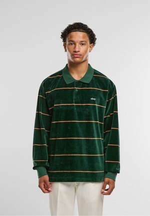 Camisa polo de felpa verde de manga larga con rayas horizontales naranjas y un cuello. Presenta un pequeño logotipo en el pecho.