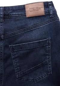 Mörkbå denimjeans med en slät yta, en enda bakficka och en brun läderetikett med "STREET ONE" och "designade med passion."
