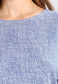 Tela de patrones azul y blanco con un diseño en forma de cuadrícula, con un escote curvado y una textura suave.