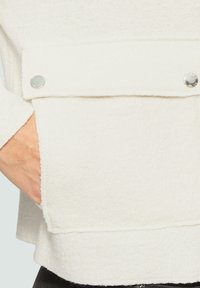 Witte fleece top met een rechte snit en een patchzak met zilveren drukknopen. Zachte textuur en een nette zoomafwerking.