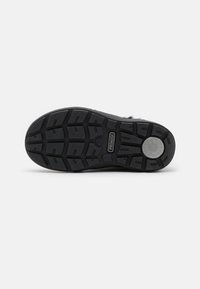 Svart gummisul med ett strukturerat mönster, innehållande spår och kanter för bättre grepp. Logotyp synlig i mitten.