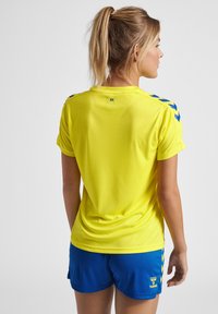 Gul sportstrøje med korte ærmer, der har blå detaljer på skuldrene, samt blå shorts. Letvægts, atletisk stof med en glat tekstur.