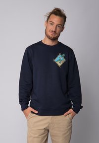 Sweatshirt bleu marine en tissu doux, avec un graphique coloré représentant une scène de plage avec des palmiers sur la poitrine. Design classique à col rond.