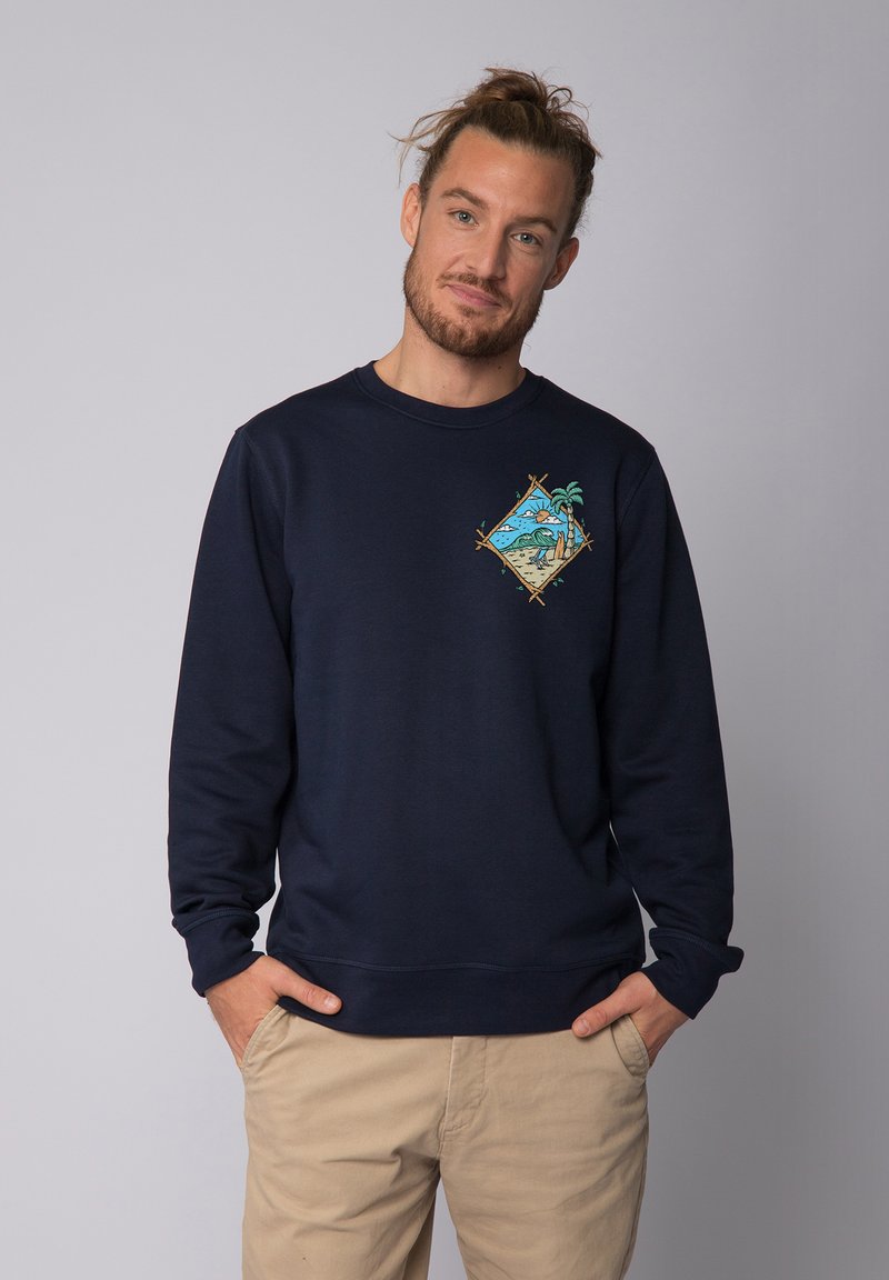 Sweatshirt bleu marine en tissu doux, avec un graphique coloré représentant une scène de plage avec des palmiers sur la poitrine. Design classique à col rond.