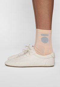 Hvide lædersneakers med en struktureret overflade, parret med ferskenfarvede sokker med et sølvfarvet cirkulært design.