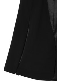 Blazer nero su misura con una texture di tessuto liscia, design strutturato, chiusura a un bottone e leggero scollo anteriore con spalline.