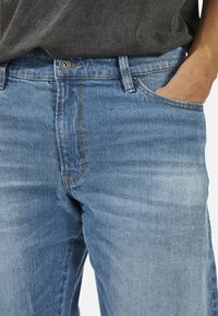 Ανοικτό μπλε τζιν παντελόνι με κλασικό σχέδιο πέντε τσεπών, αντίθετη πορτοκαλί ραφή και κούμπωμα στη μέση.