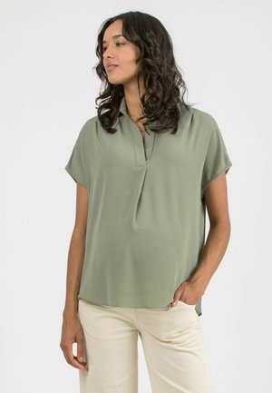 Olive green blouse made of smooth fabric, featuring a buttonless collar, short sleeves, a relaxed fit, and side slits at the hem.