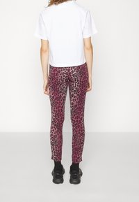 Person standing facing away wearing a white short-sleeve top, pink and black leopard print leggings, black socks, and black sneakers.