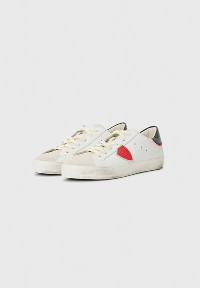 Baskets en cuir blanc avec un accent rouge, un bout en suède beige et un talon noir. Dotées de lacets plats et d'une semelle en caoutchouc légèrement usée.
