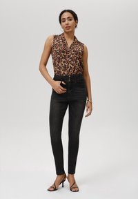 Blusa sin mangas de estampado de leopardo, jeans skinny negros de cintura alta y tacones negros con tiras. Diseño limpio, textura suave, forma ajustada.