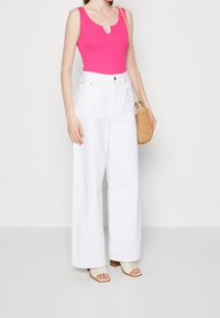 Różowy bezrękawnik z dekoltem w serek, w połączeniu z białymi spodniami o wysokim stanie i szerokimi nogawkami oraz jasnymi sandałami na obcasie.