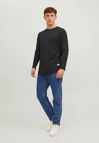 Μαύρο μακρυμάνικο τοπ από βαμβάκι, σε συνδυασμό με μπλε τζιν τζην. Παπούτσια λευκά αθλητικά. Απλός σχεδιασμός με στρογγυλή λαιμόκοψη και χωρίς σχέδια.