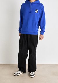 Kunga blå hoodie med känguruficka, ribbad manschett och snörad huva. Bärs med svarta löst sittande byxor och mönstrade sneakers.