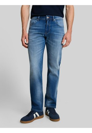 Man wearing blue faded straight-leg jeans and navy blue sneakers with white stripes on a grey background.