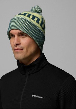 Berretto lavorato a maglia blu e giallo con un pompon sulla sommità e una texture a costine; il testo del logo è presente in modo prominente attorno al bordo.