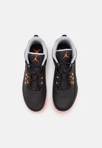 Paire de chaussures de basketball noires avec des œillets orange, logo orange sur la languette, et semelles blanches et orange vues de dessus sur fond blanc.