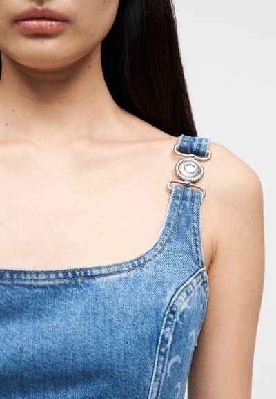 Τζιν φόρεμα με φαρδιές τιράντες, ανοιχτό μπλε χρώμα και ασημένια κουμπιά στη χιαστή. Διαθέτει υφή και καμπυλωτή λαιμόκοψη.