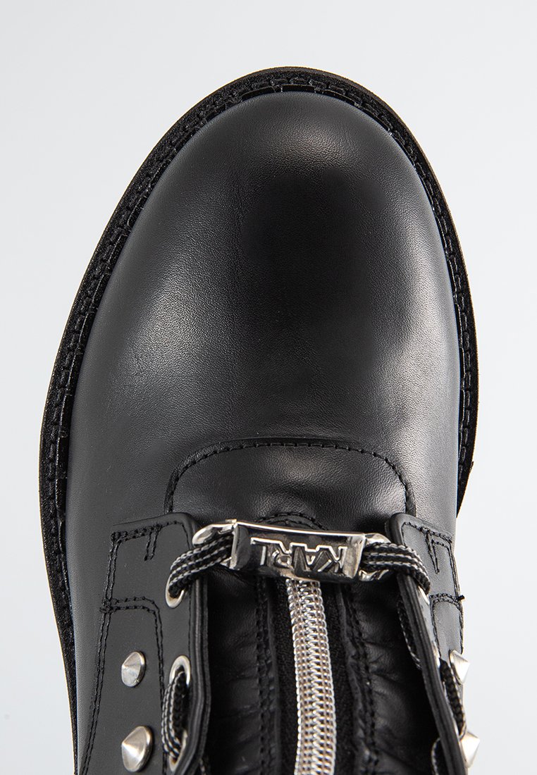 Botte en cuir noir avec un nez rond, fermeture éclair argentée, rivets décoratifs, accents texturés et couture contrastante le long de la semelle.