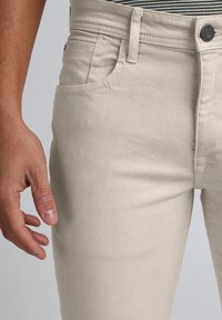 Pantaloni bej din bumbac, croială slim, cu design clasic cu cinci buzunare. Textură netedă cu detalii subtile de cusături și închidere cu nasture în talie.