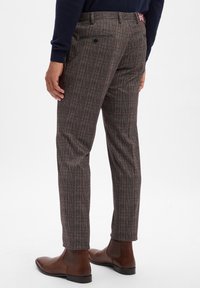 Men's plaid trousers made of textured fabric, featuring brown, red, and blue patterns, with two back pockets and brown ankle boots.