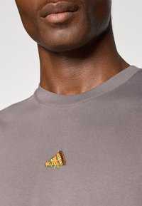 Szürke pamut póló, amelyen elöl egy kis, színes pizzaszelet hímzés található díszítő részletként.