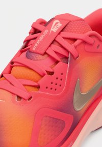 Baskets de sport rose vif avec un design dégradé, tige en maille et synthétique, lacets texturés et logo Nike métallique.