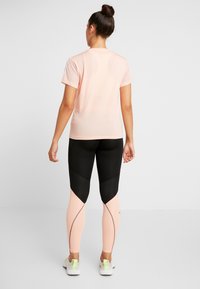 Světlé růžové sportovní tričko s průsvitnými síťovanými rukávy, doplněné černými a světle růžovými legínami s geometrickými barevnými bloky a kontrastním prošíváním.