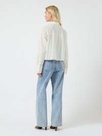 White cropped shirt with a back yoke, paired with light blue high-waisted wide-leg jeans and brown heeled shoes, viewed from the back.