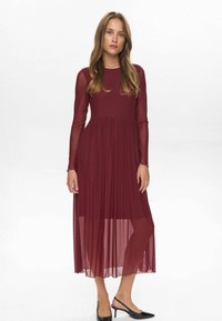 Rochie lungă burgundy cu mâneci lungi, având un top texturat și o fustă fluidă, transparentă. Rochia are un corset ajustat și este până la gleznă.