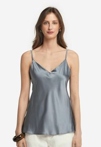 Grå satinlinne med tunna justerbara axelband, V-ringning och slät textur. Bärs med ett mörkt armband runt handleden.