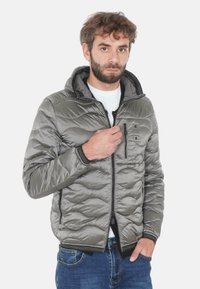 Giacca imbottita grigia con cappuccio, frontale con cerniera e superficie testurizzata. Include una tasca sul petto e rifiniture nere su polsini e orlo.