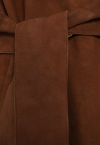 Barna szarvasbőr anyag, sima tapintású, középen megkötött övvel díszítve, tiszta, jól látható varrási szélekkel.