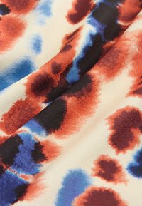 Abstraktna tkanina s kremno podlago in akvarelnim vzorcem s madeži rdeče, modre in črne barve. Mehka tekstura, lahka tkanina.