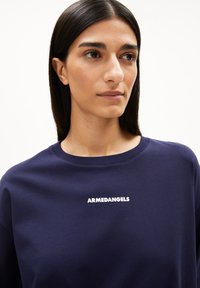 Marineblauwe katoenen T-shirt met een ronde hals, voorzien van witte "ARMEDANGELS" tekst gecentreerd op de borst, een gladde textuur en een ontspannen pasvorm.