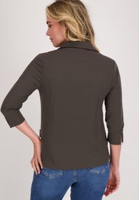 Bruine driekwartmouwen shirt met een getailleerd ontwerp, een gladde textuur en zijsplitten bij de manchetten, gecombineerd met blauwe jeans.