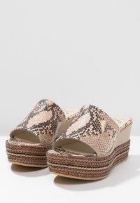 Kilklackssandaletter med ett ormskinnsmönster i nyanser av beige och brunt, med öppen tå och flätad jute-liknande plattform för textur.