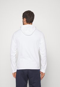Witte hoodie met lange mouwen en een gebogen zoom, met een gladde textuur. De achterkant toont een minimalistisch ontworpen capuchon.