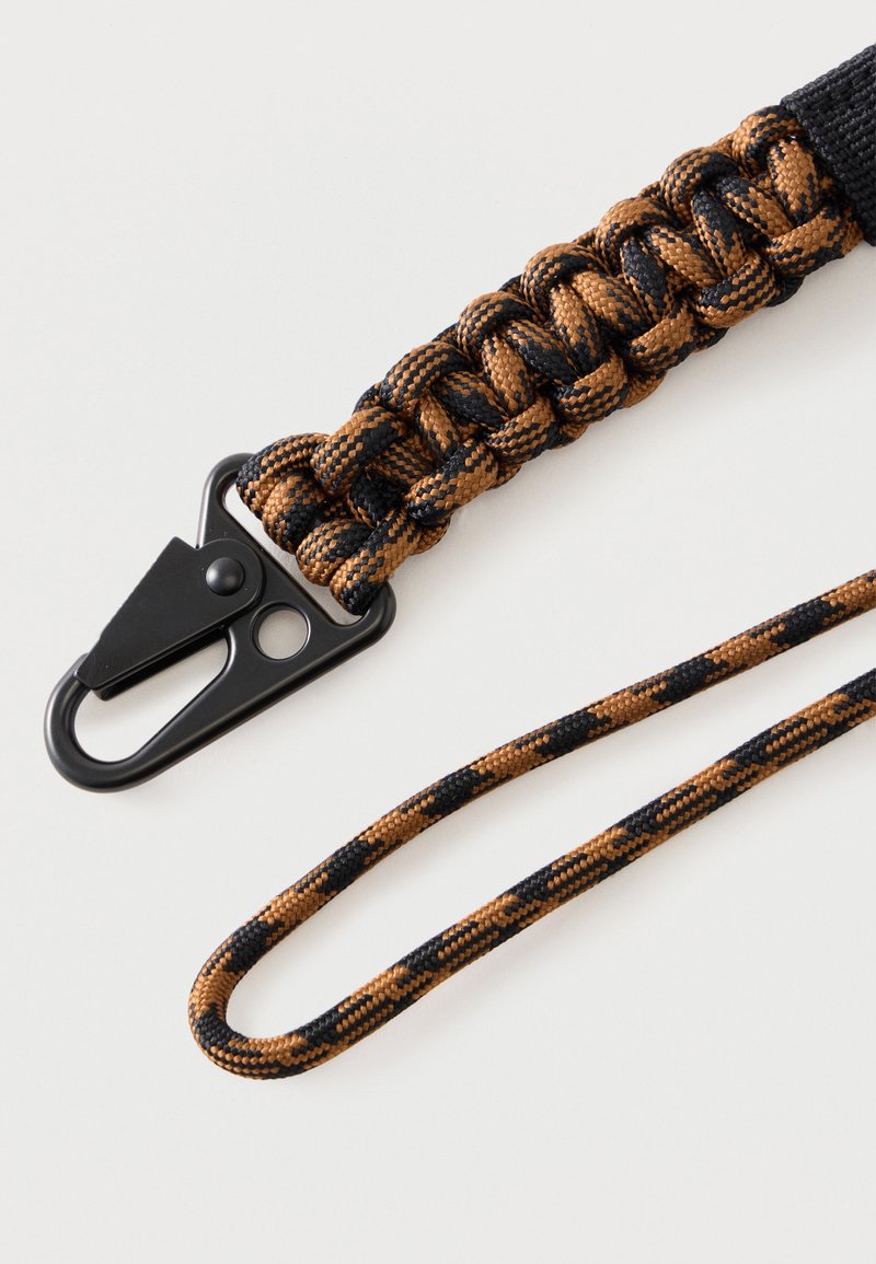 Flettet brun og sort paracord rem med sort metal karabinerlås og matchende nøglesnor på hvid baggrund.