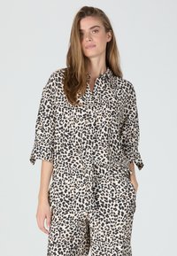 Leopard print shirt made of lightweight fabric, featuring a button-up front, collar, and loose sleeves, paired with matching pants.
