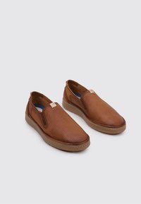 Zapatos marrones tipo slip-on con parte superior de cuero perforado, suela de goma color marrón claro, paneles laterales elásticos y una pequeña etiqueta de marca cerca de la abertura.