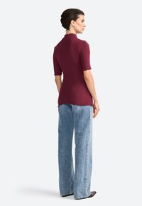 Top bordeaux à côtes avec des manches courtes, col festonné et ourlet, associé à un jean en denim bleu clair à jambes larges, porté avec des chaussures à bout pointu.