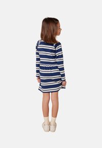 Gestreiftes Kleid in Marineblau und Weiß, mit langen Ärmeln, gerafftem Taillenbund, schwingendem Rock, weichem Stoff, kombiniert mit cremefarbenen Schuhen und Socken.